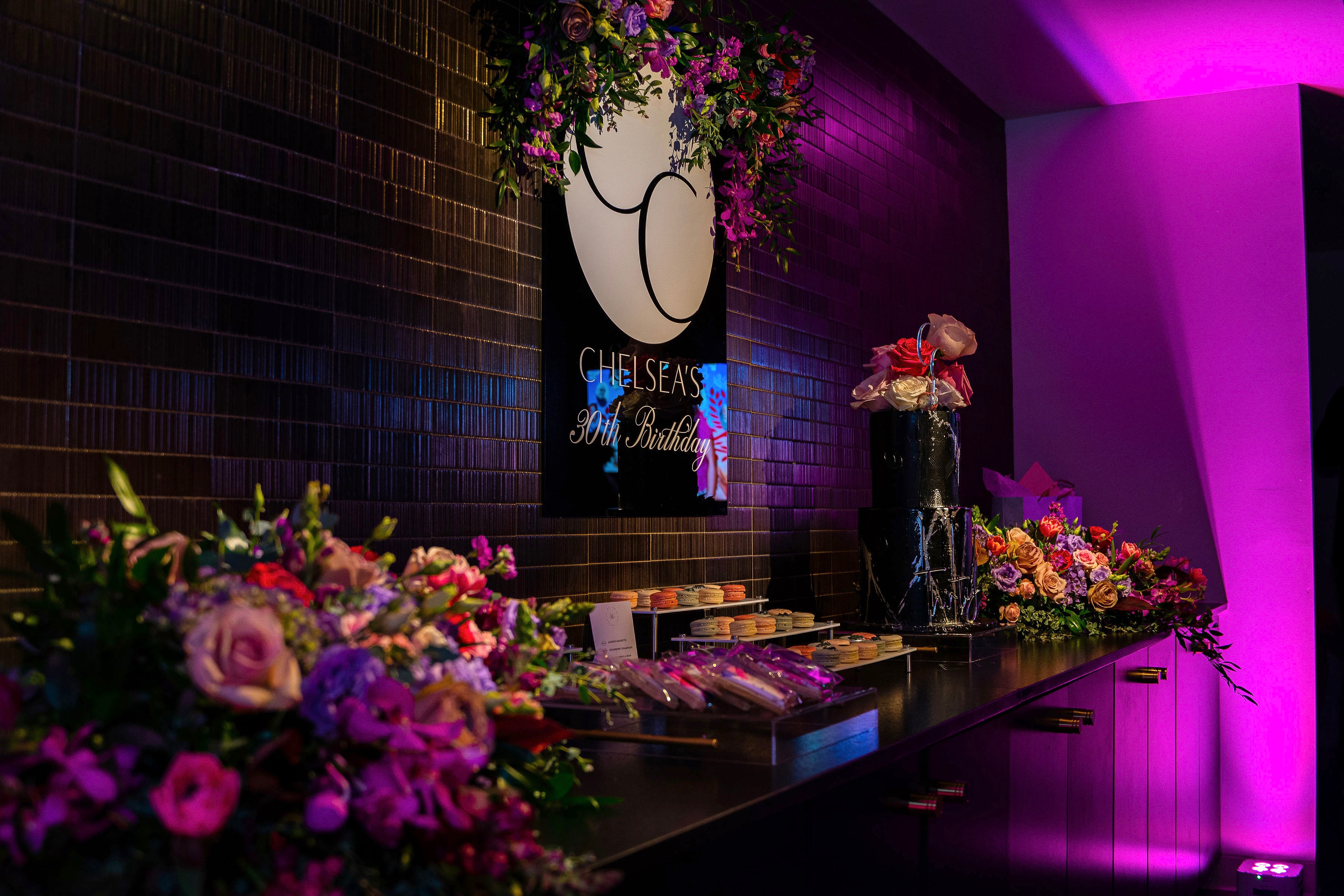 An elegantly decorated venue for Chelsea's 30th birthday celebration, featuring floral arrangements and personalized gifts, showcases meticulous event planning.