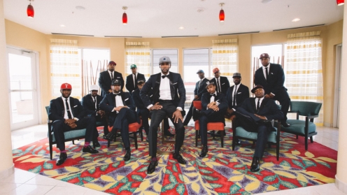 Group of men in formal attire with matching hats sitting and standing in an elegant room.
