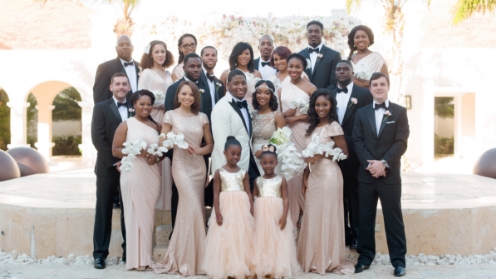 A wedding party posing for a group photo, with the bride and groom at the center, surrounded by bridesmaids in matching dresses, groomsmen in formal attire, and flower girls.
