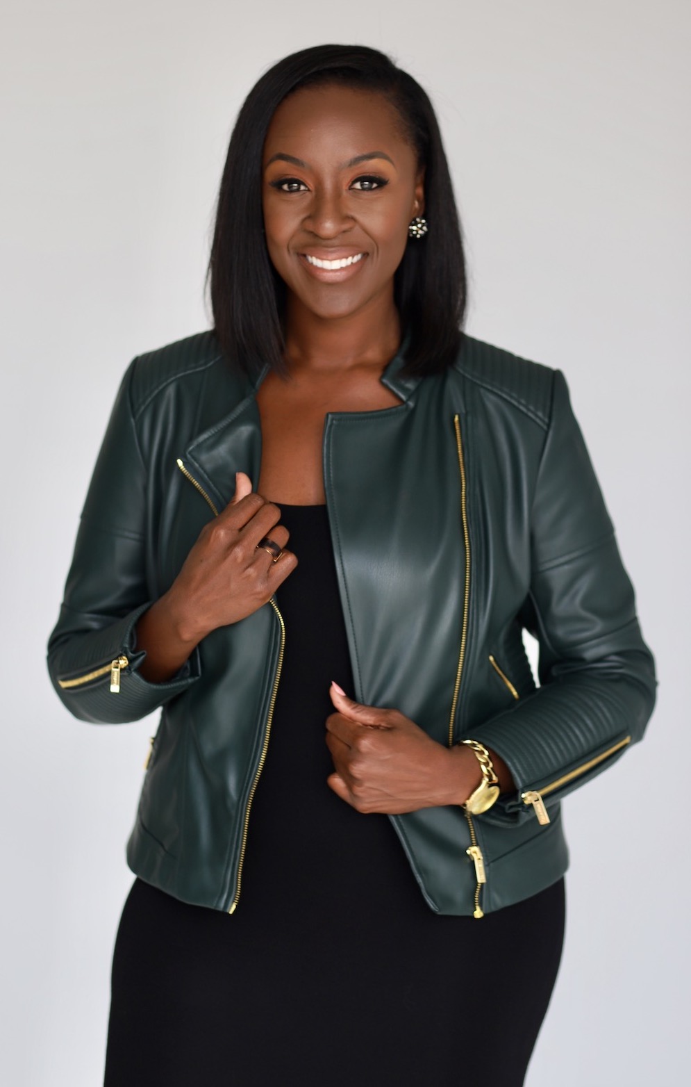 Confident woman in a black dress and green leather jacket smiling at the camera.